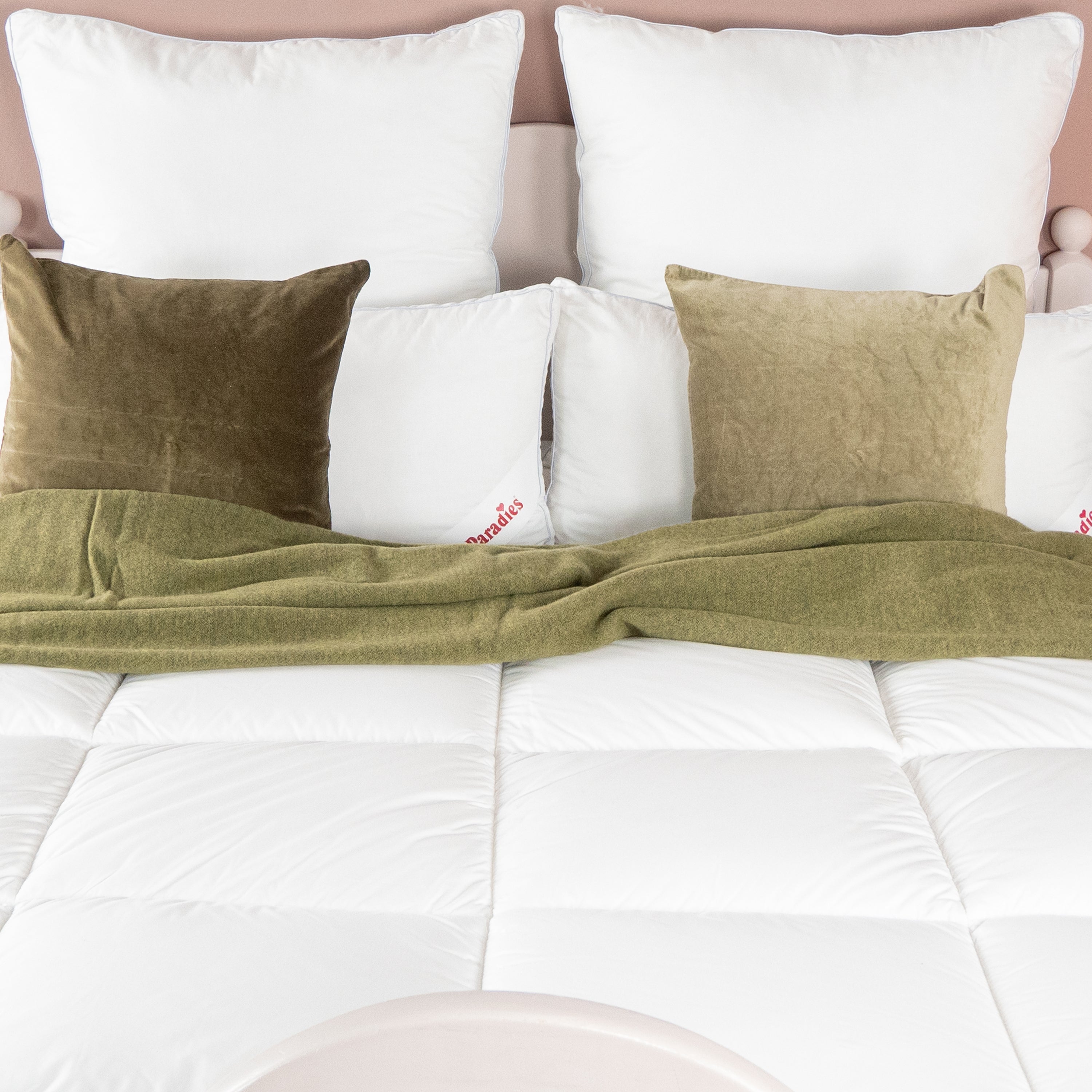 Weißes Bett mit zwei großen weißen Paradies Kissen, zwei kleineren weißen Kissen und zwei grünen Samtkissen, grüner Überwurf auf weißer Avera Winterdecke