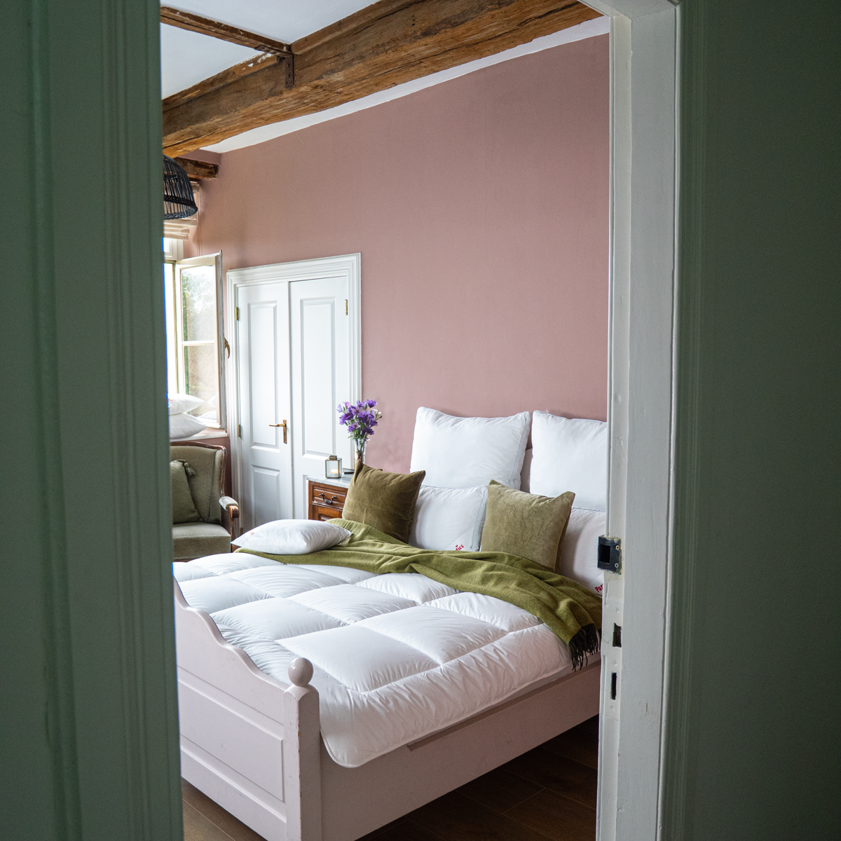 Avera Winterbettdecke dekoriert mit grüner Decke und Kissen in einem Schlafzimmer mit rosa Wand und Holzbalken an der Zimmerdecke