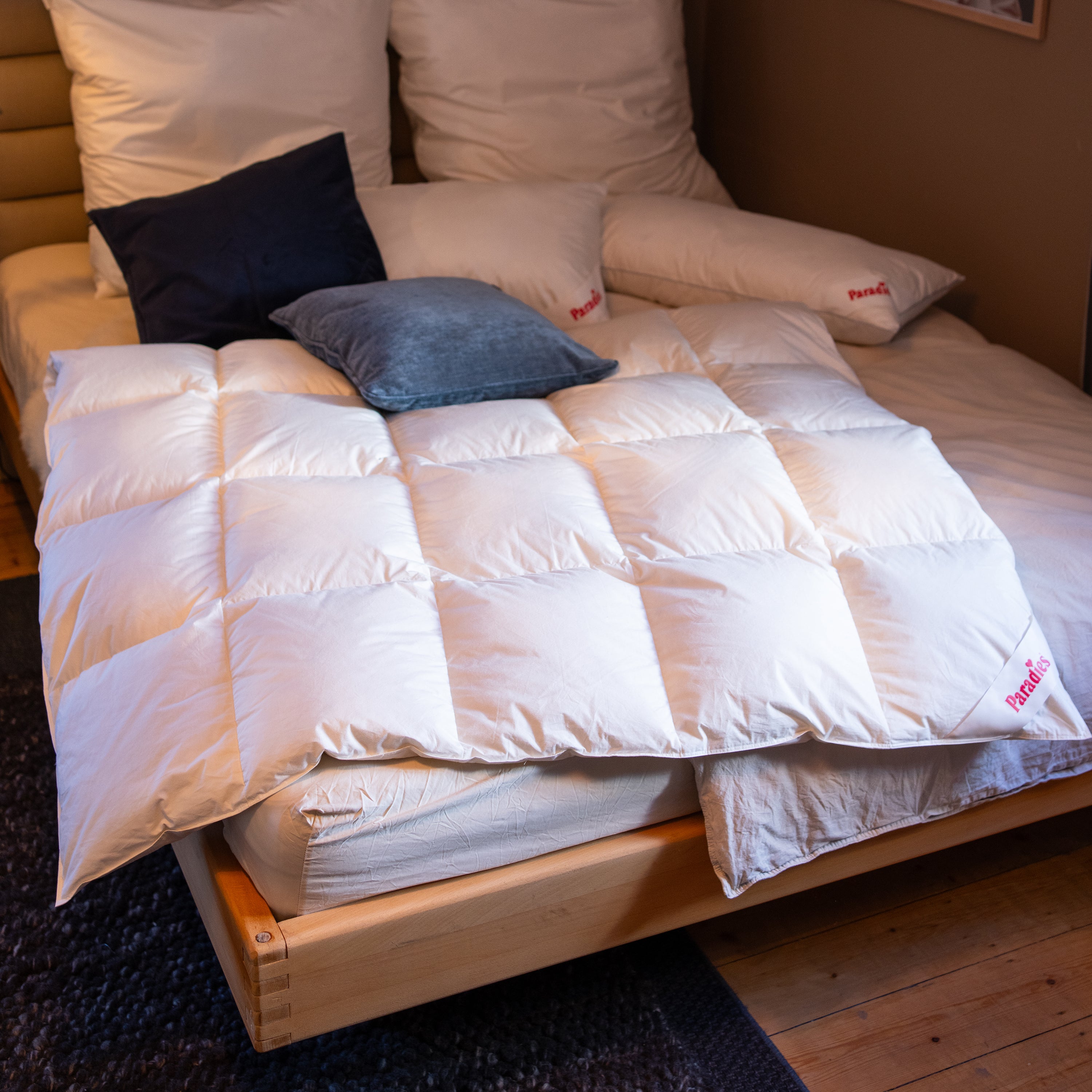 Weiße Paradies Daunendecke auf einem Holzrahmenbett mit mehreren Kissen in Grau- und Weißtönen