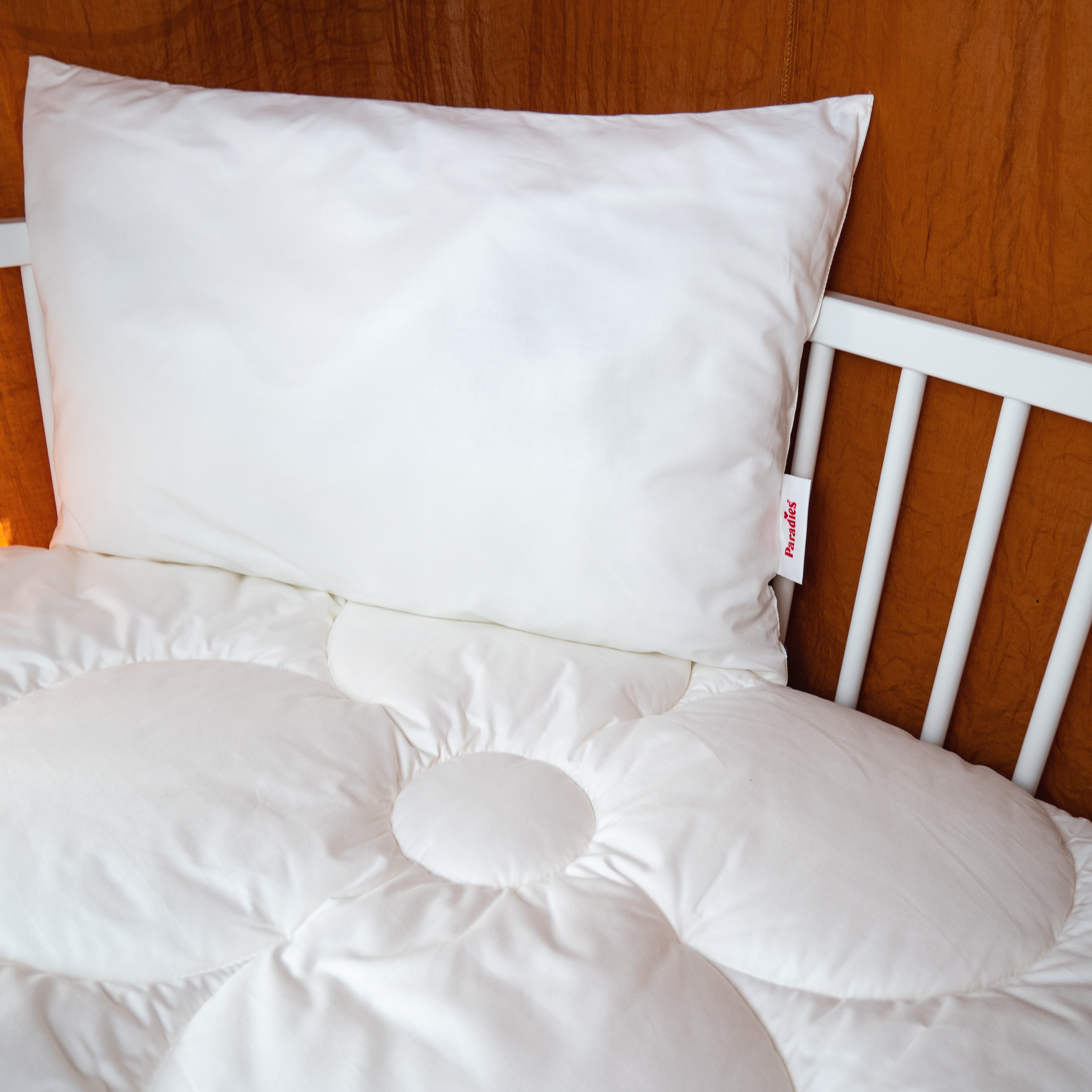 Weißes Kinderkopfkissen auf einem weißen Gitterbett mit Holzwand im Hintergrund
