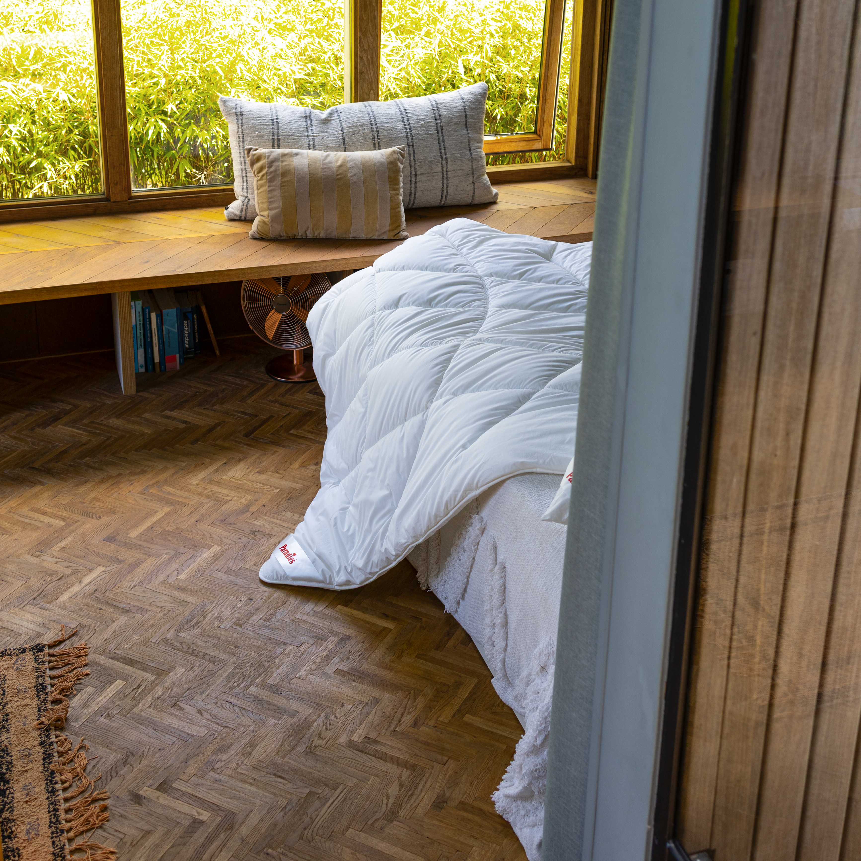 Die weiße Paradies Runa Bio Ganzjahresbettdecke liegt sanft auf dem Bett und reicht bis auf den Holzfußboden.