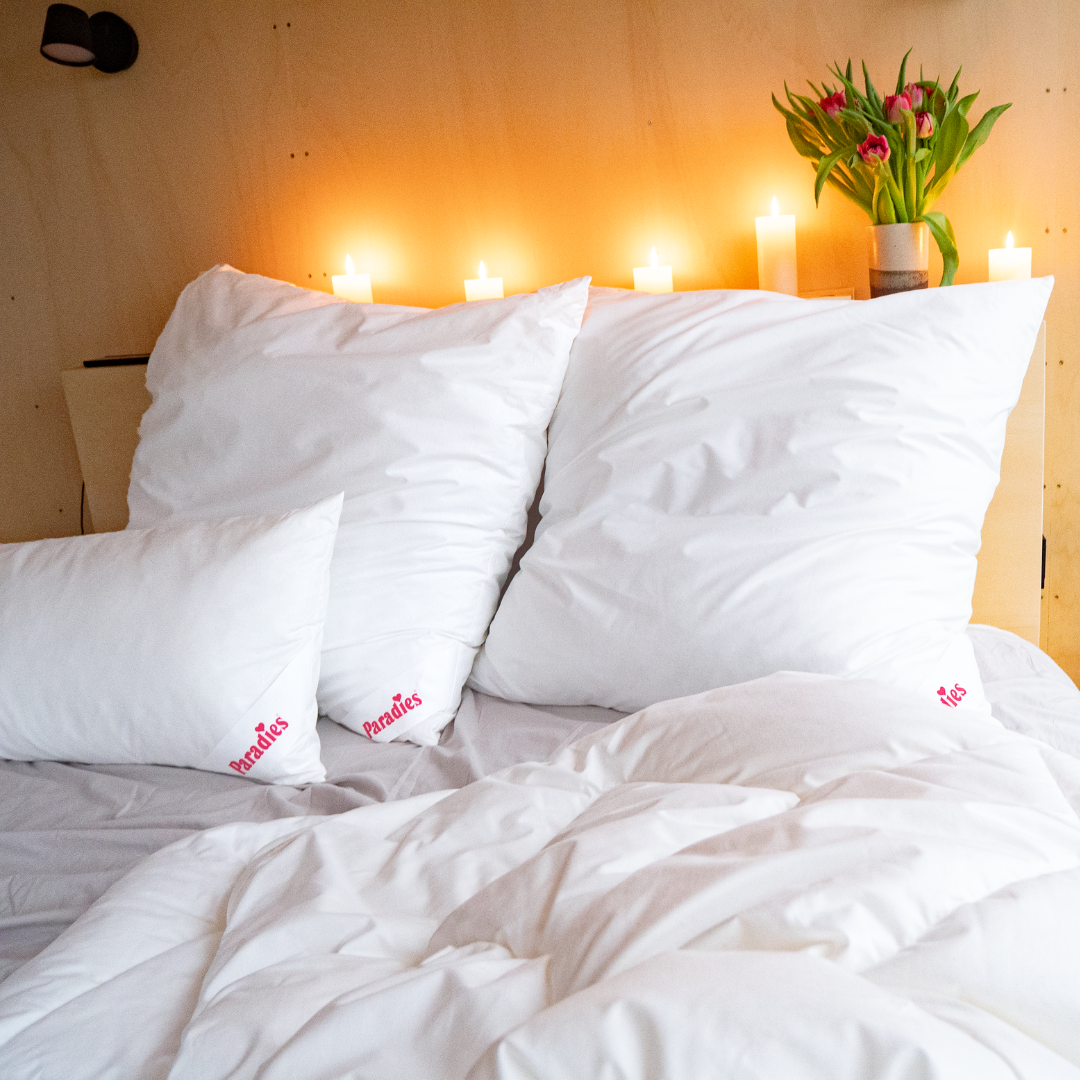 Drei weiße Paradies Softy Top medium Kissen auf einem Bett mit weißer Bettdecke, Kerzen und Blumen im Hintergrund
