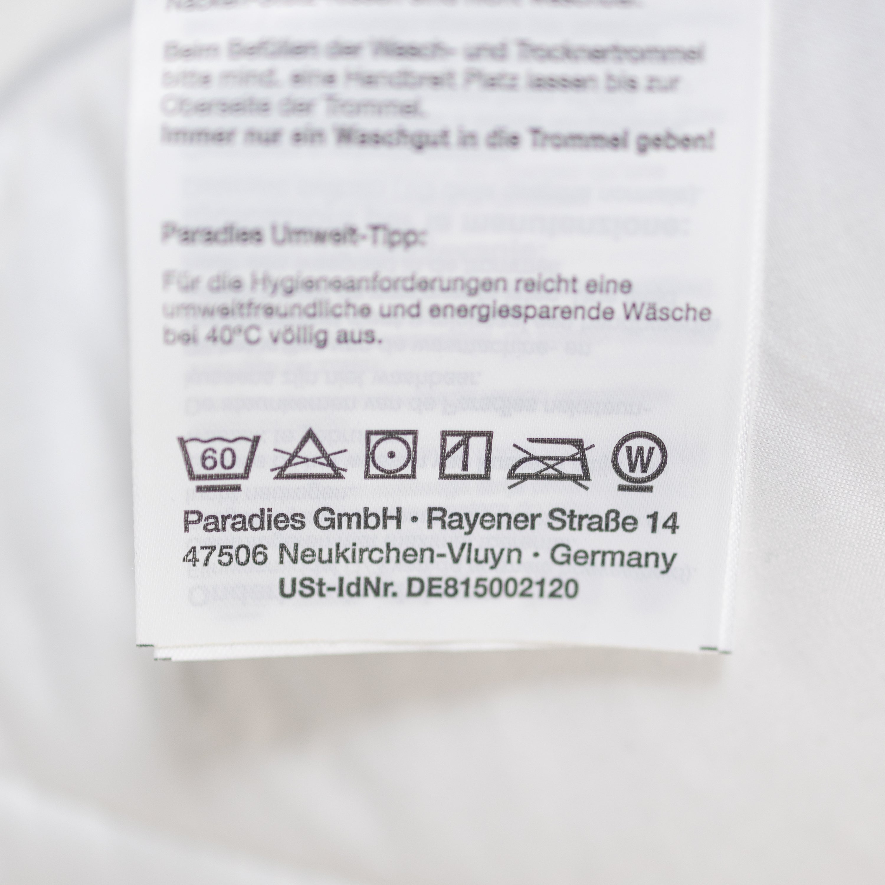 Pflegehinweise auf einem weißen Textil-Etikett mit Waschsymbolen und Herstellerangaben von Paradies