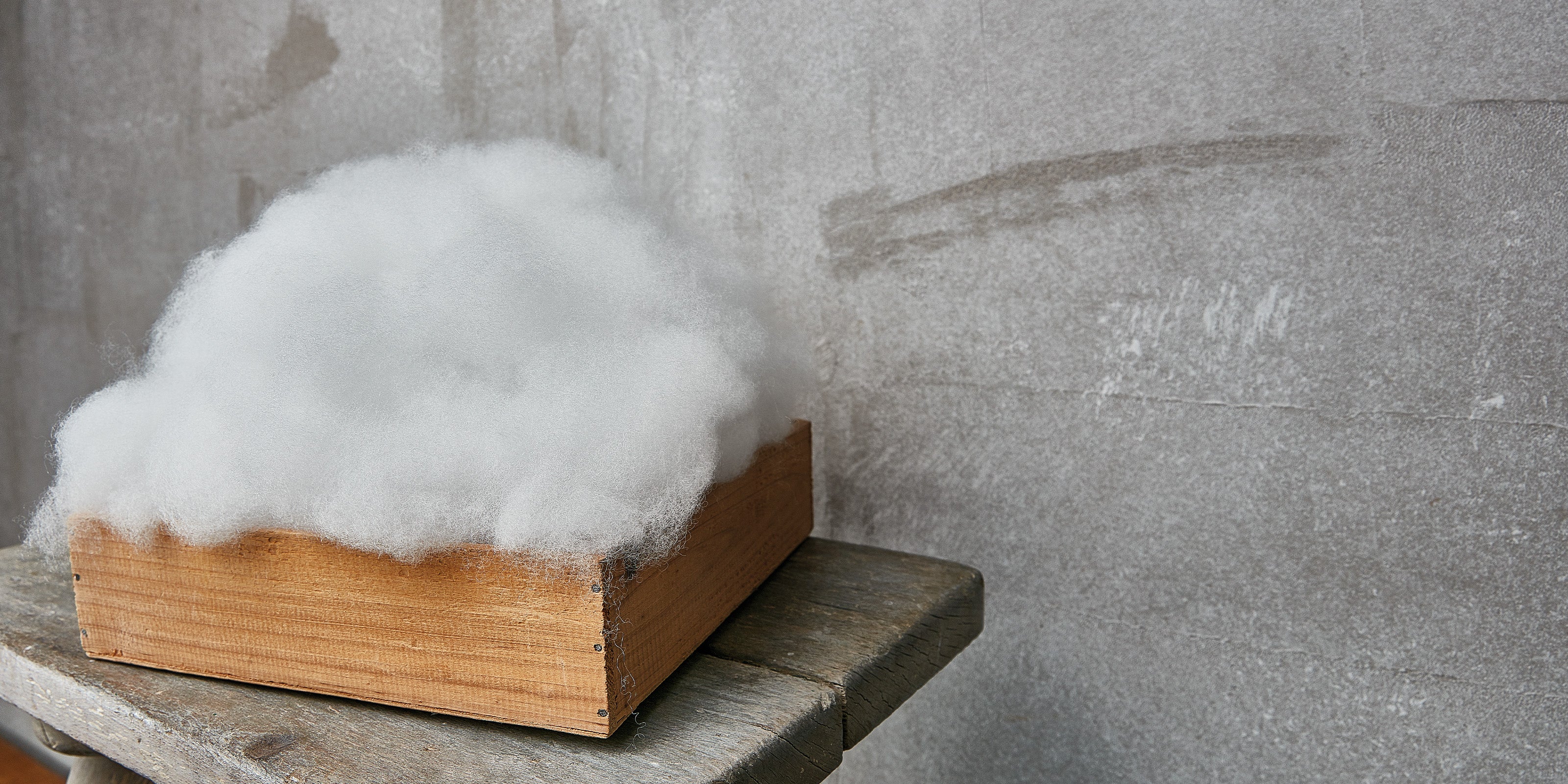 Holzkiste gefüllt mit weißem, flauschigem Textilfasermaterial vor grauer Wand
