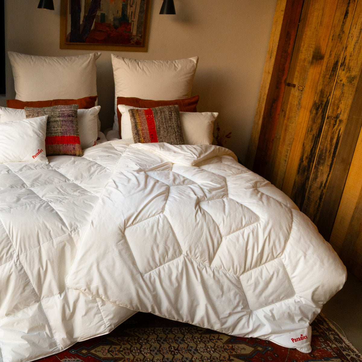 Doppelbett mit weißer Steppdecke und mehreren Kissen vor einer Holzpaneelwand